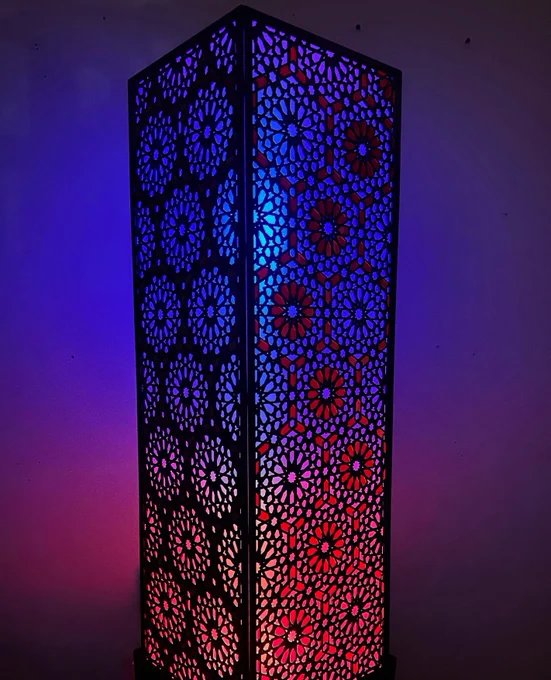 Intricately designed illuminated lantern with geometric patterns, glowing in vibrant blue, purple, and red hues against a dark background.