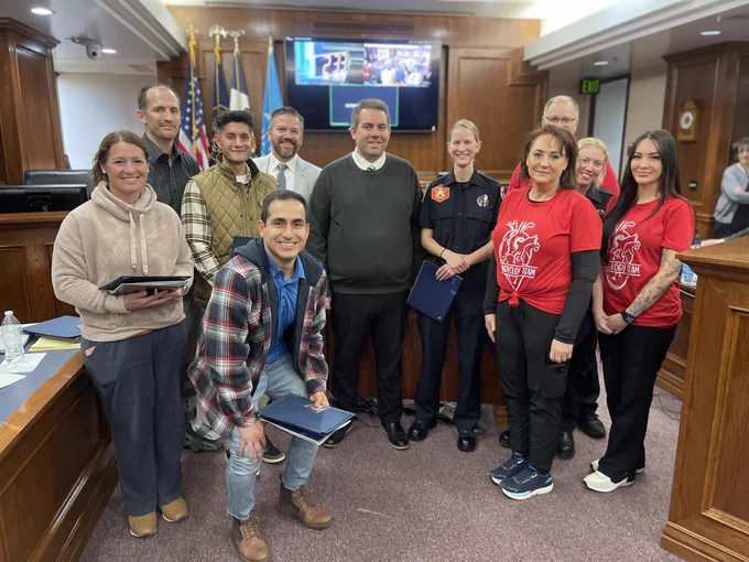 Bystanders, Spanish Fork Fire EMS responders, and dedicated medical professionals from the Cath Lab at MountainStar Healthcare’s Mountain View Hospital in Payson, Utah, pose together as a group, smiling, with two Utah County Commissioners and their recognition awards for saving a patient's life.