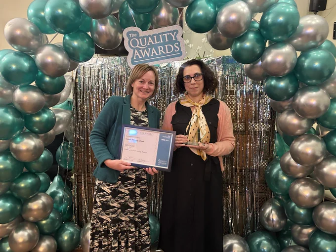 two women smiling, holding a certificate in front of a balloon arch.
