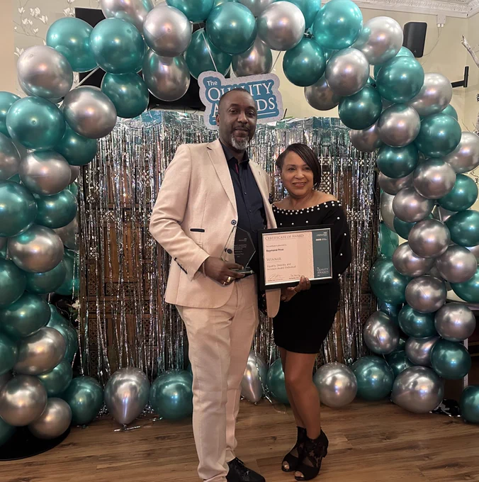 two people smiling in front of a balloon arch.