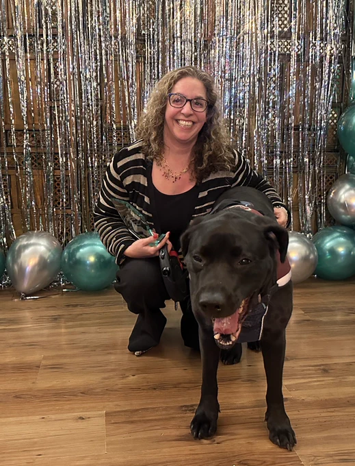 a woman and dog smiling in front of a balloon arch.