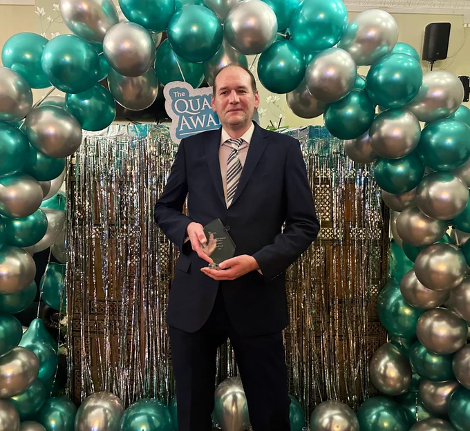 A man smiling in front of a balloon arch.