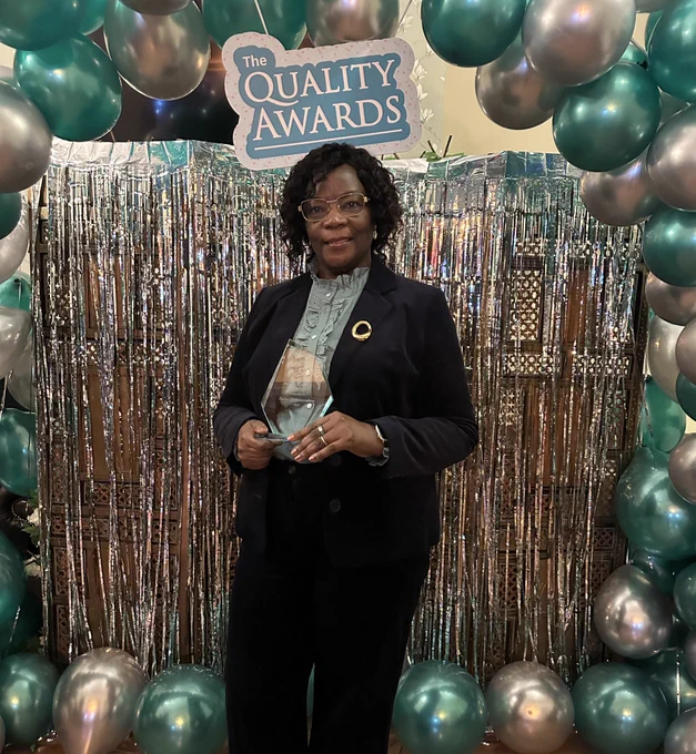 woman smiling wearing glasses and holding a trophy.