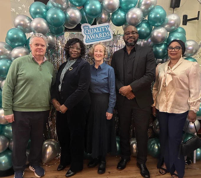 five people smiling in front of a balloon arch.