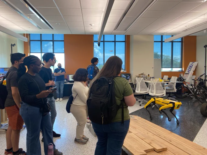 People attending an exhibition in a bright indoor space with various engineering projects on display, including a robotics setup and a bike.