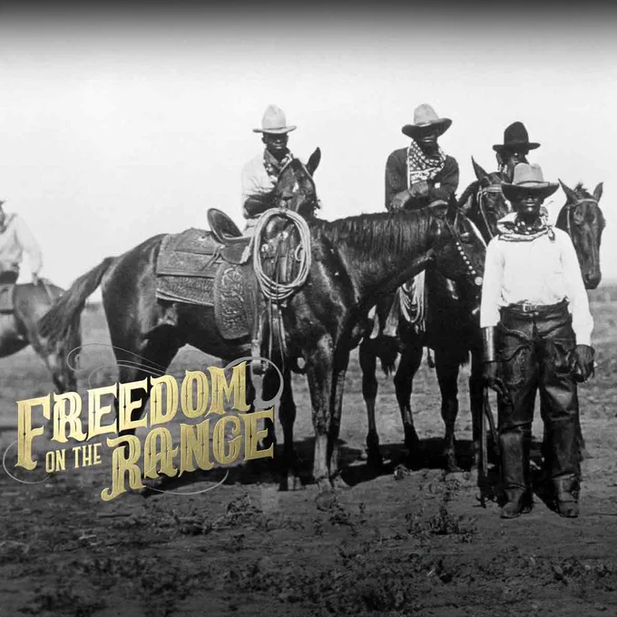 A group of four Black cowboys stand facing the camera with three atop their horses as the last looks on while standing on the ground in a black and white photo.
