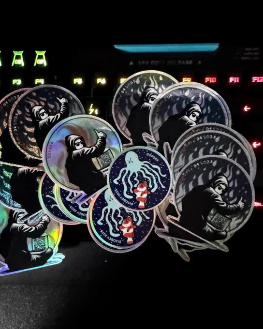 A colourful keyboard with a stack of round stickers on top, featuring a design of a hooded person sitting at a laptop.