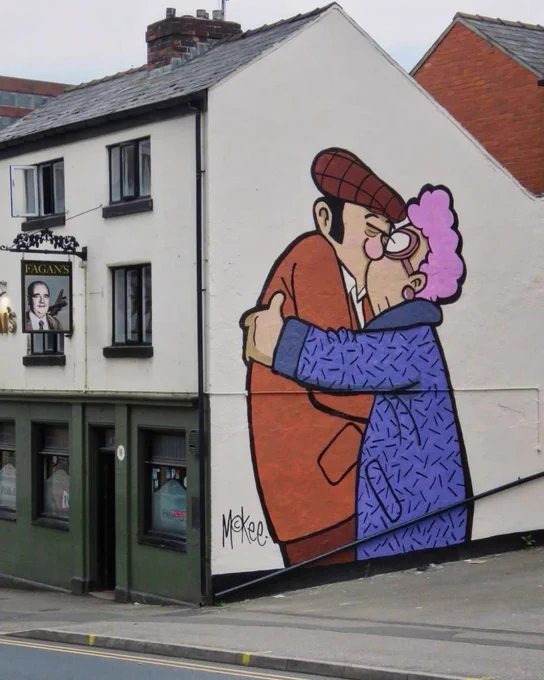A vibrant mural illustrating an elderly couple kissing, located on the side of a prominent pub in Sheffield