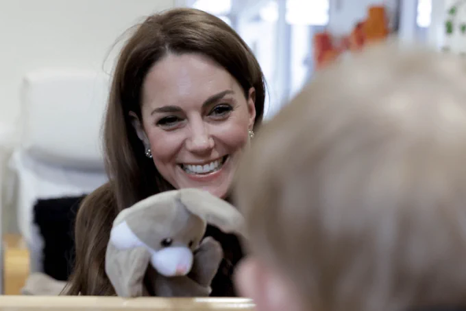The Princes of Wales smiling while holding a puppet during a playful interaction with a child.
