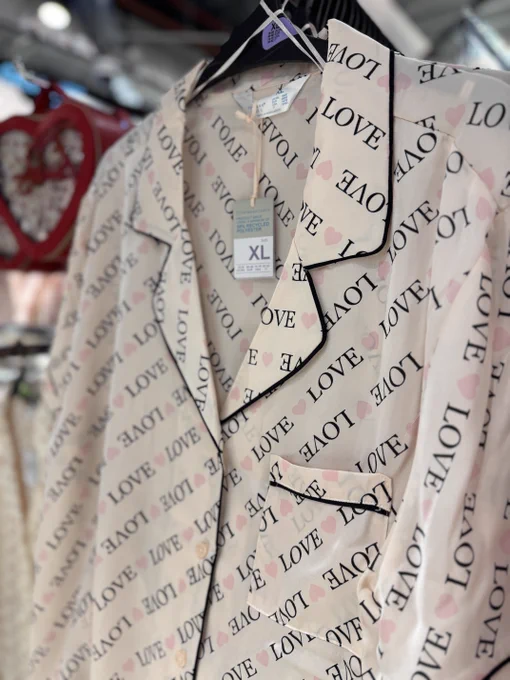 Close-up view of a beige jacket with a repeating "LOVE" pattern, displayed in a store. The size tag XL is visible on the jacket.