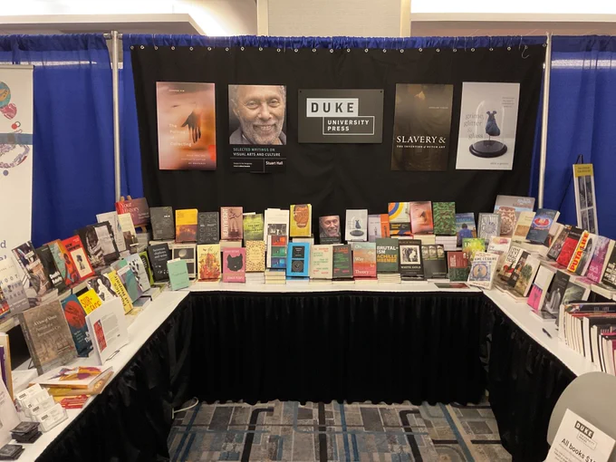 The DUP booth displays a “U” of varied books beneath a series of posters and the Duke University Press logo.