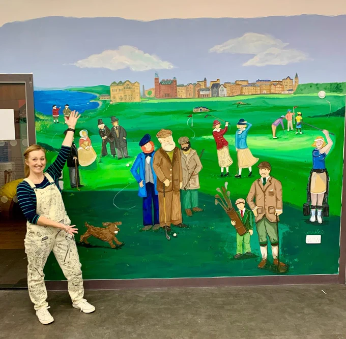 A female artist stands next to her finished painted wall mural.  
