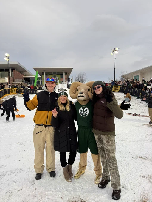 President Parsons, CAM the Ram, and two others pose for a picture in front of the ski slope. They are all smiling at the camera.