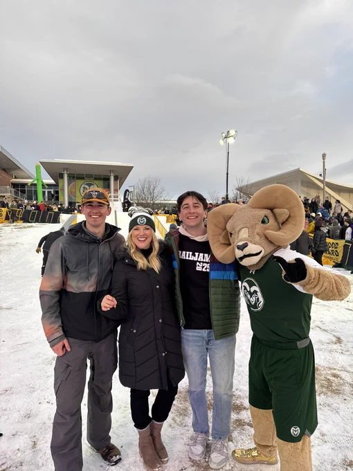 President Parsons, CAM the Ram, and two members of ASCSU pose for a picture in front of the ski slope. They are all smiling at the camera.