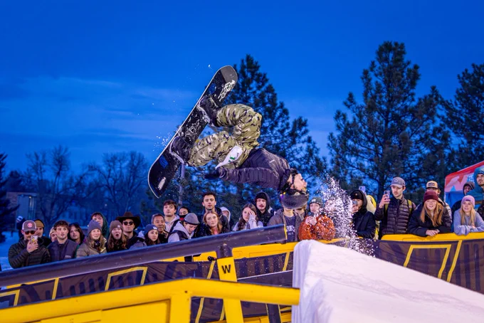 A snowboarder doing a backflip mid air at Rail Jam.