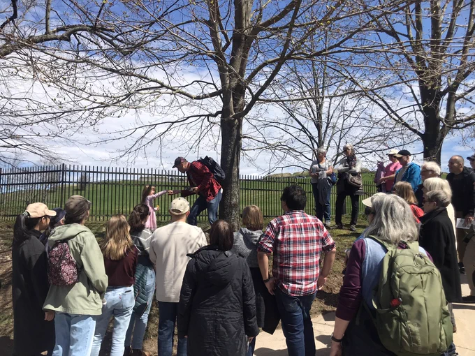A group of people surround a young girl who is passing a rock to a tour leader during an urban geology tour.