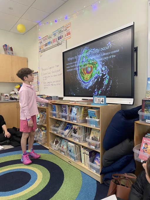Student stands in front of smart bird with presentation titled where do hurricanes mostly occur