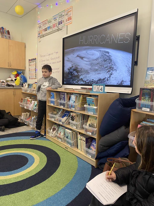Student stands in front of smart bird with presentation titled hurricanes