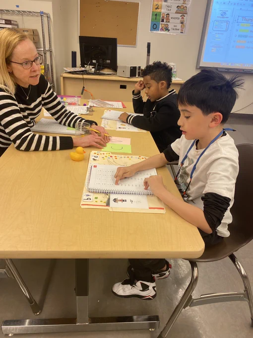 Students sit with a teacher and read word lists