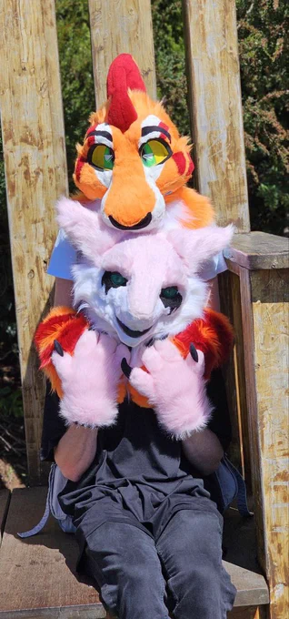 Two fursuiting sitting together, one sitting behind the older with their head resting ontop of the one In front posing for a photo