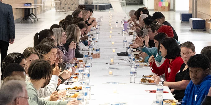 People eat together at a long table at the Community Table event at the Jacobs School.