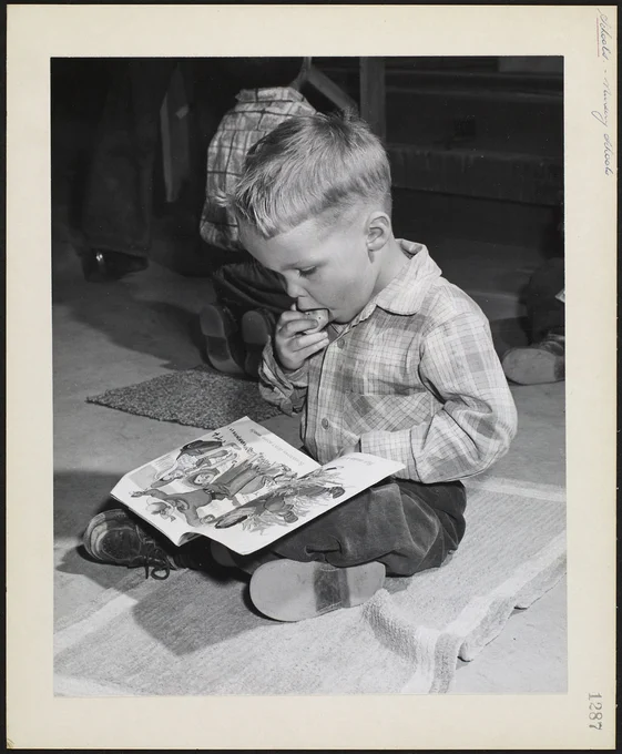 Stevie Farthing reading a book and eating a biscuit at Salaberry Co-op Nursery School, Montreal, Quebec