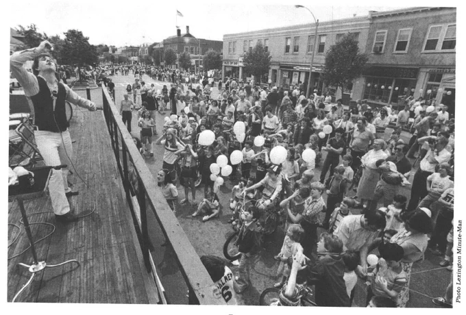 Black and white photo of a large crowd in the street watching a performer onstage