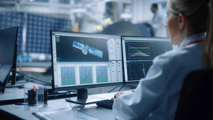 Scientist sitting at a desk analysising satellite data on computer screens in front of them.