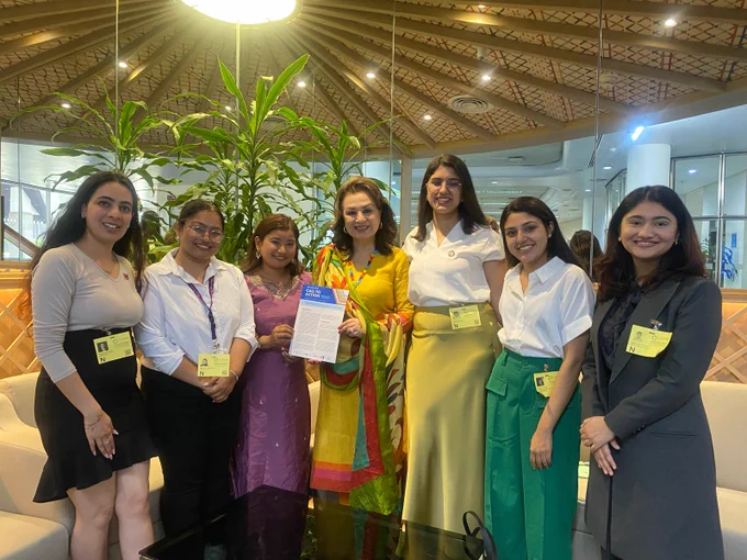 Seven people in a group photo where third girl from left side in handing over a Youth Call to Action to Bandana Rana who is at the middle of the photo. 