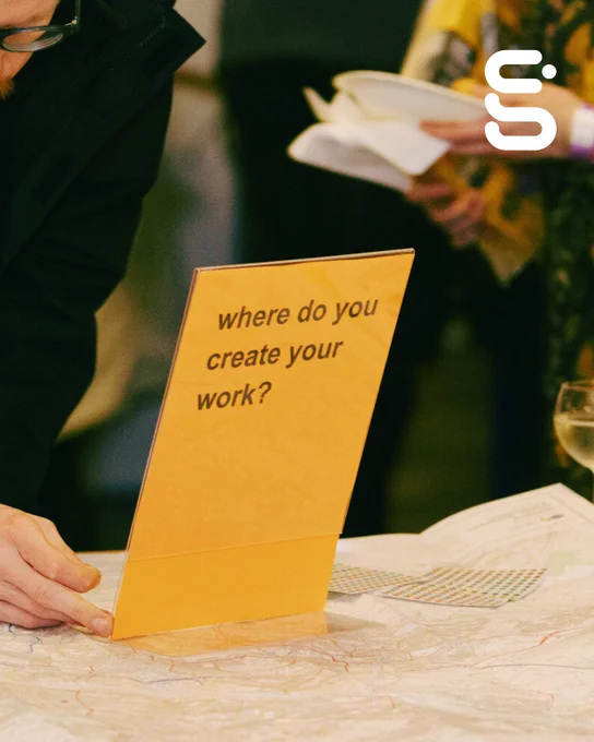 A person bends over a map next to a sign that reads "where do you create your work?"