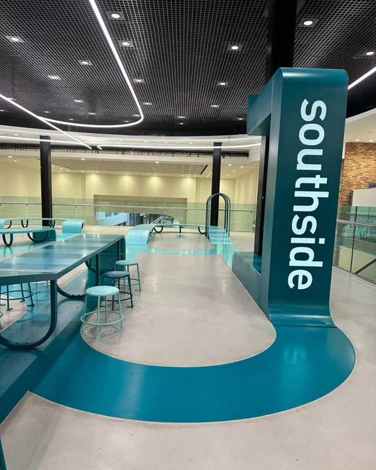 Interior of Southside shopping centre with modern design, featuring curving blue paths, matching tables, and unique column signage.