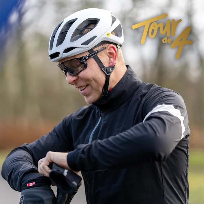Sir Chris Hoy in cycling gear wearing a helmet adjusts his watch outside, with the 'Tour de 4' logo visible in the corner.