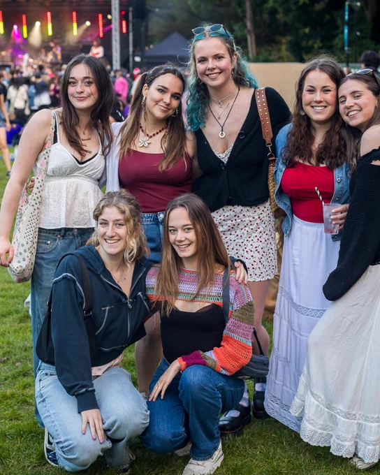 Image of seven students smiling at the camera at Valefest with a performance taking place in the background.