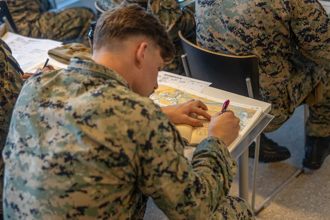 A Marine writes in a notebook on top of a chart that is on a desk. (Photo Credit: Lance Cpl. Christian Salazar, U.S. Marine Corps Forces, Europe and Africa)