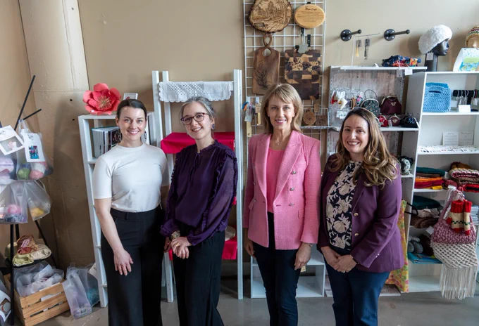 Four individuals standing in a store filled with craft supplies and handmade items, smiling at the camera.
