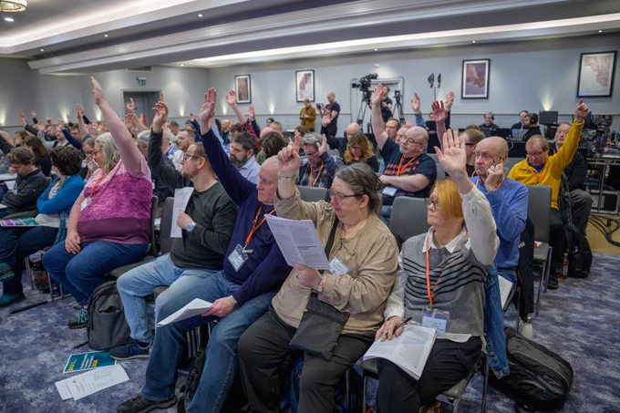 An image of the delegates with their hands in the air voting on a motion