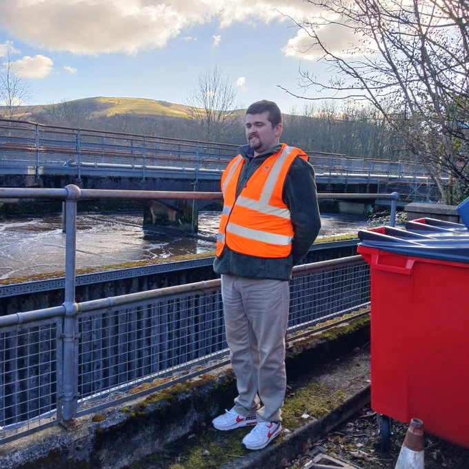 wearing a high visibility orange vest and looking out at part of the water treatment centre