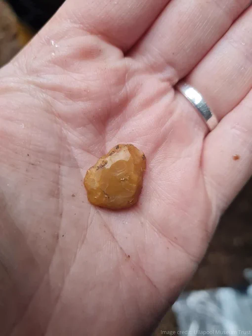 Hand holding a small yellow chipped piece of flint  