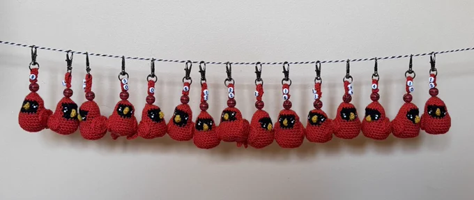 15 crochet cardinal keychains hang on a rope. Each has a basketball player’s number on them.