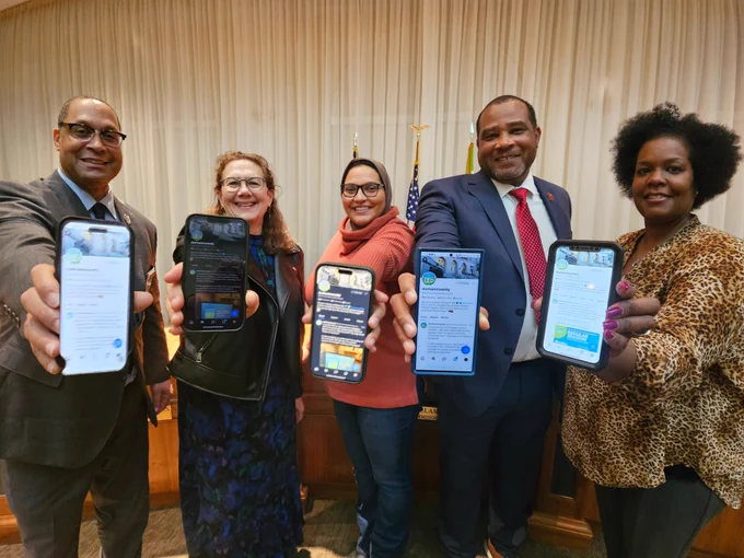 Durham Board of County Commissioners hold up their phones showing the official Durham County Government account on Bluesky.