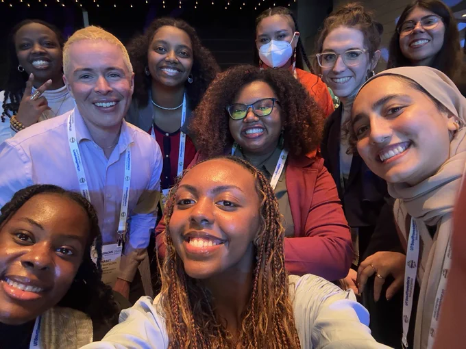 A group selfie of the 2024-25 cohort of MINDS post-baccalaureate scholars and their program director at the 2024 ABRCMS conference. This group of scientists are all dressed up in conference attire and smiling widely for the photo.
