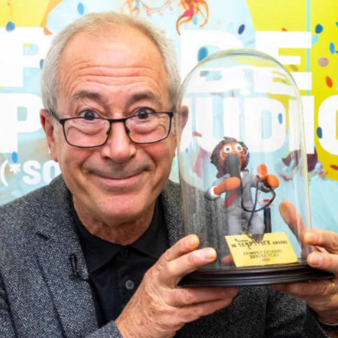 Ben Elton (wearing a grey blazer and black shirt) holding the Aardman Slapstick Comedy Legend award 