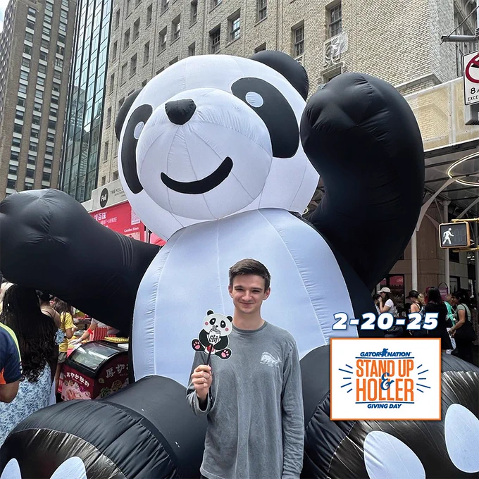 Asa Worden holds small panda art on a stick posing in front of a large inflatable panda.

"2-20-25"
"Gator Nation Stand Up & Holler Giving Day"