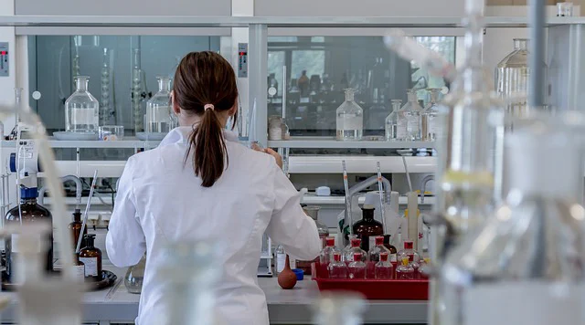 Scientist in a lab coat and a low pony tall standing at a lab bench.