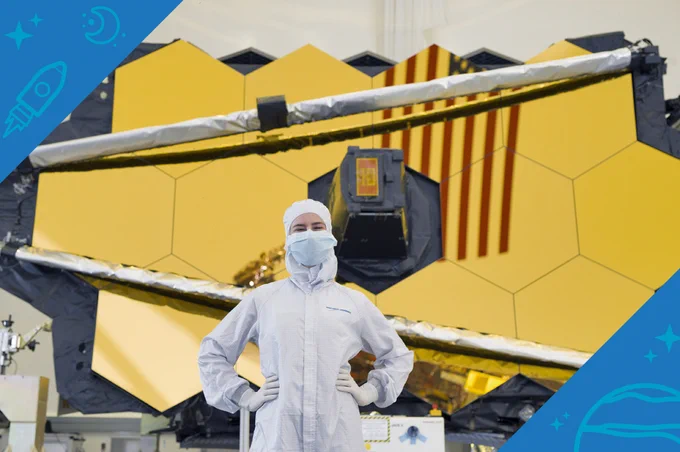 Elaine Stewart, a contamination control engineer, wears a white clean room suit and mask & poses with her hands on her hips in front of the gold mirrors of NASA's James Webb Space Telescope