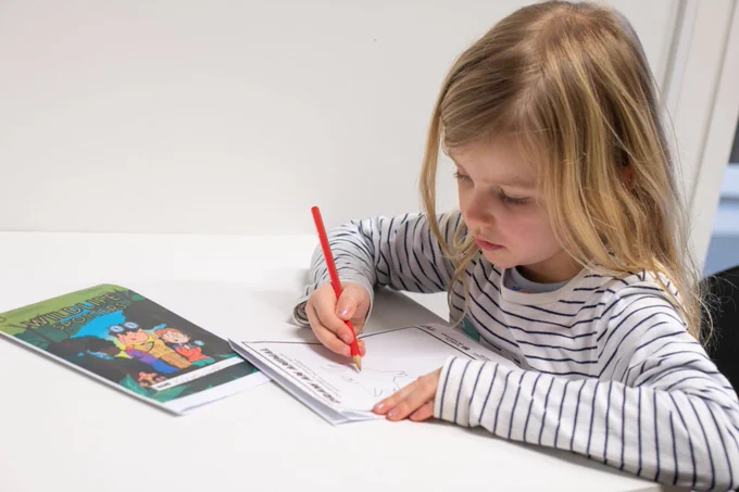 A child wearing a white and black striped top, sitting down and writing with pencil and paper.