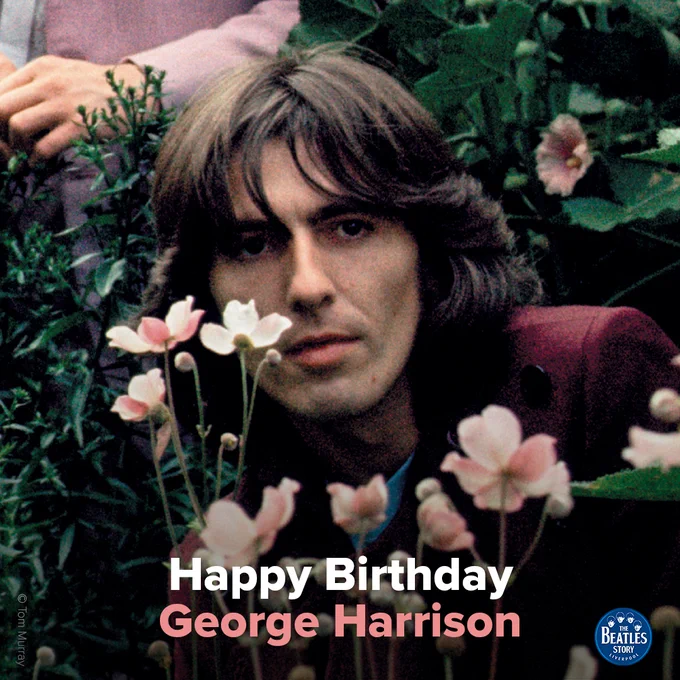 a photo of george harrison at the beatles' mad day out photoshoot in nineteen sixty eight. he is wearing a maroon blazer and is surrounded by pink flowers and foliage. text at the bottom of the image reads "happy birthday george harrison"