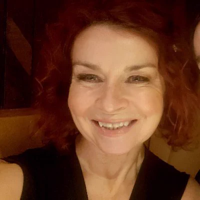 A photo of a woman with reddish-brown curly hair, smiling widely