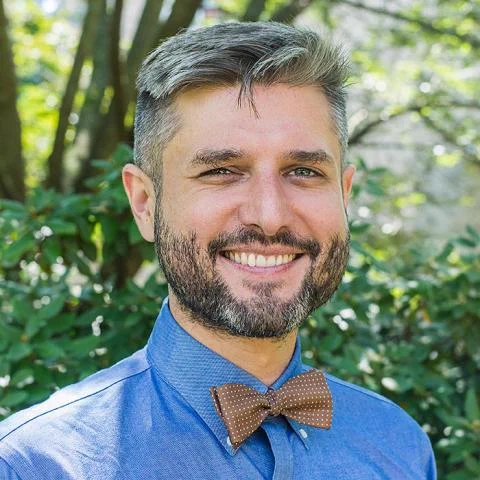 Photo of Matthew Farmer, smiling at the camera, with greenery in the background.