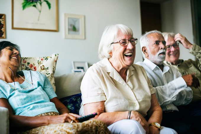 Photo of group of older people sat on sofa together and laughing